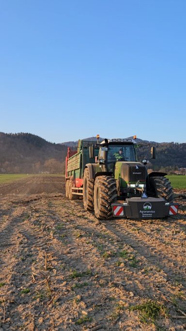 Großer Traktor in einem Feld, Sonnenlicht und Berge im Hintergrund.